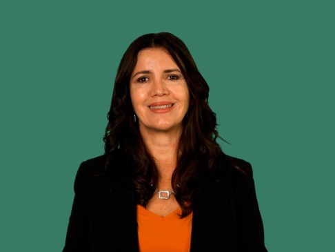 Woman standing in front of a green background wearing a black business jacket and orange top