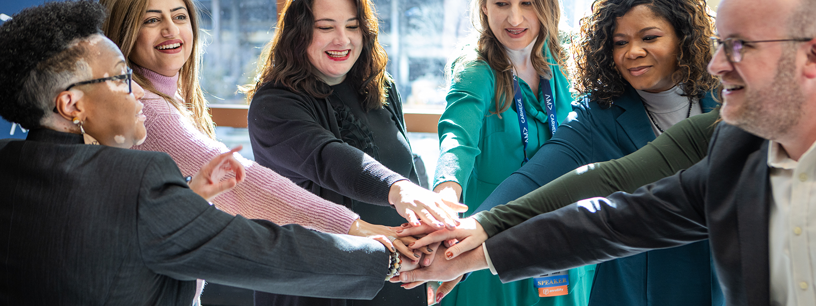 Group of attendees at AMA's Higher Ed conference putting their hands in the middle of a circle as they prep for a cheer.